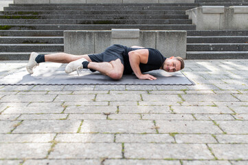 Young man doing a spider push-up or side kick push-up outdoor on concrete background in the city