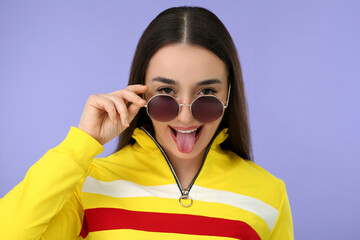 Happy woman in sunglasses showing her tongue on violet background - obrazy, fototapety, plakaty