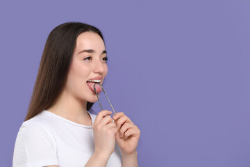 Happy woman brushing her tongue with cleaner on violet background, space for text - obrazy, fototapety, plakaty