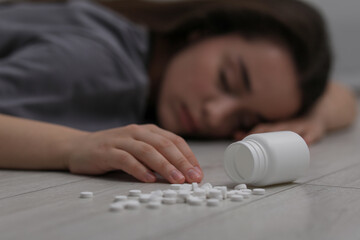 Woman sleeping near overturned bottle with antidepressants on floor indoors, selective focus