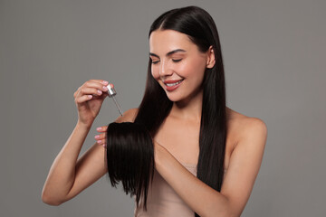 Beautiful woman applying hair serum on grey background. Cosmetic product