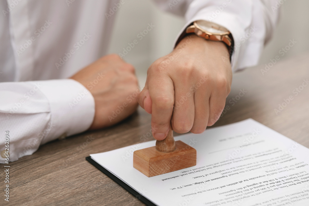 Sticker Man stamping document at wooden table, closeup