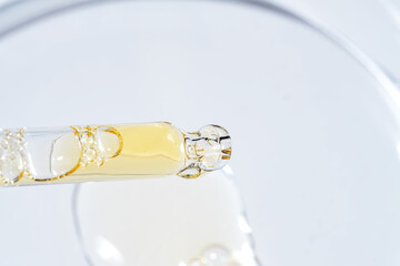 Face serum drops in a in petri dish on blue background. Face oil pipette dropper. Beauty facial...
