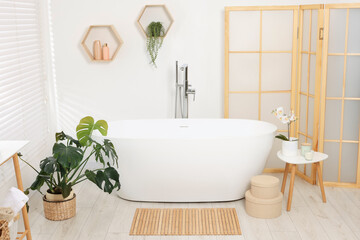 Fototapeta na wymiar Stylish bathroom interior with bath tub, houseplants and bamboo mat