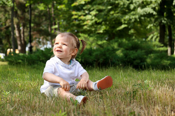 Cute girl sitting on grass in park, space for text