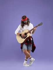 Stylish hippie man in sunglasses playing guitar on violet background