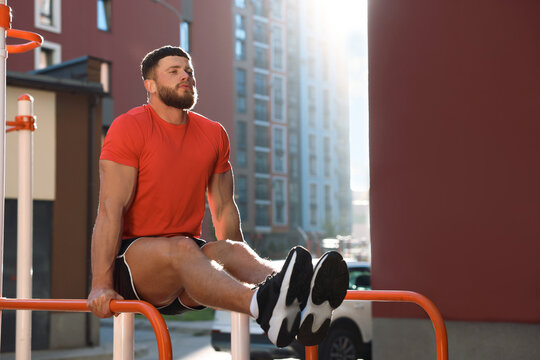 Man training on parallel bars at outdoor gym on sunny day