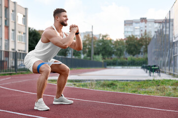 Muscular man doing exercise with elastic resistance band at stadium
