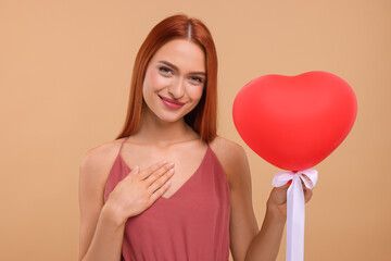 Beautiful woman with red heart shaped balloon on beige background