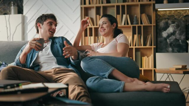 Smiling pair talking couch holding cups coffee. Couple relaxing family evening