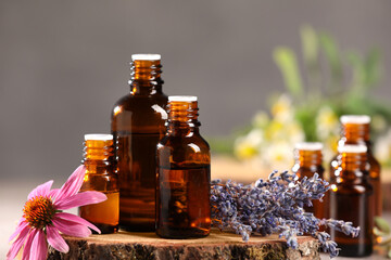 Bottles with essential oils and flowers on blurred background, closeup