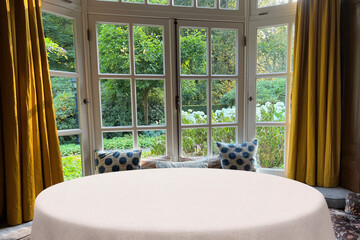 Empty table with white tablecloth against window indoors. Space for design