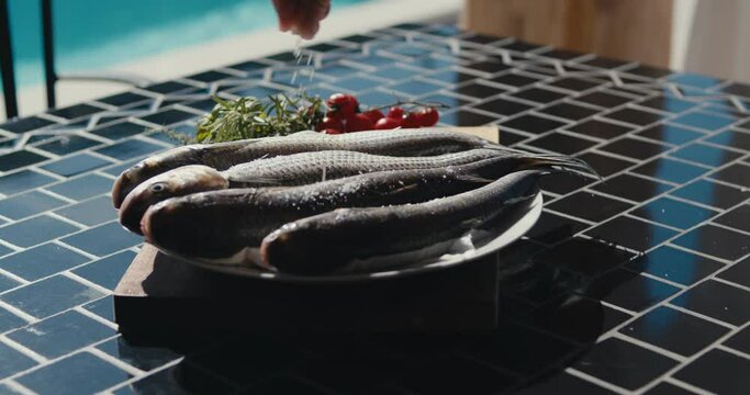 Female hand salt olive oil seasons fresh raw mullet fish in close up