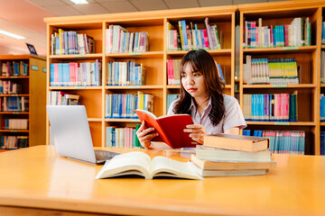 Asian female university student sitting at table with books and laptop in library