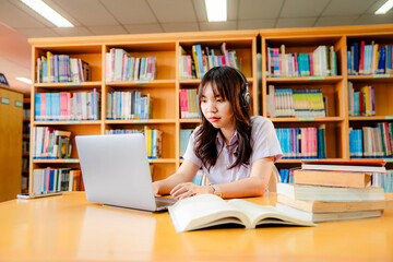 Asian female university student sitting at table with books and laptop in library