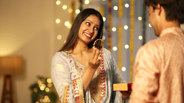 Happy young Indian man giving surprise bangle gift to wife during diwali festival.she is very happy.Indian woman getting a precious gift from her loving husband during the festival celebrations.