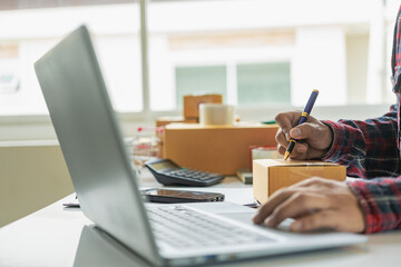 Fototapeta premium Small business startup SME business owners use smartphones or tablets to receive and monitor online orders to prepare product boxes for delivery. Close-up pictures