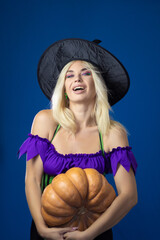 Blonde woman in a witch costume holding pumpkin in her hands