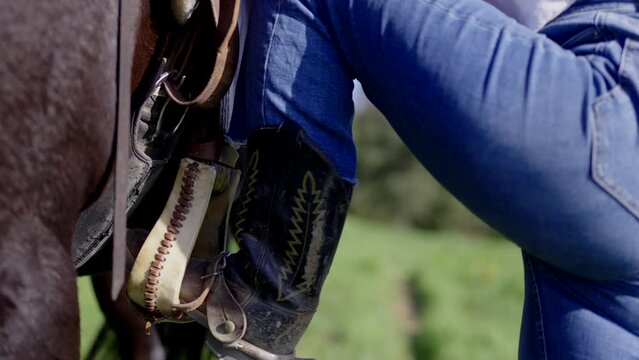 Closeup of unrecognizable person getting on the horse using the stirrup