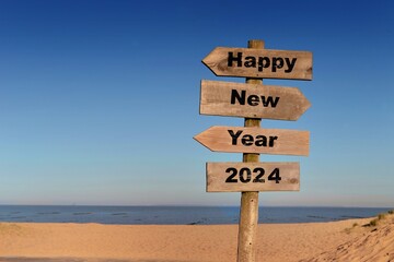 2024 happy new year written on a direction sign in front of a beach on blue sky
