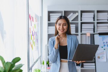 Asian business woman standing holding laptop in office.