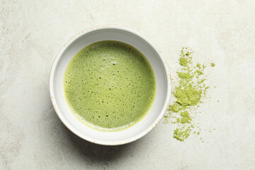 Cup of fresh matcha tea and green powder on light grey table, top view