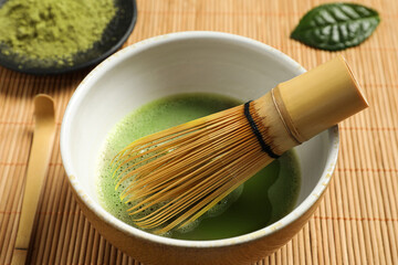 Cup of fresh green matcha tea with whisk and spoon on bamboo mat, closeup
