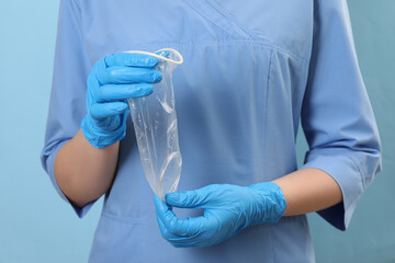 Doctor with unrolled female condom on light blue background, closeup. Safe sex - obrazy, fototapety, plakaty