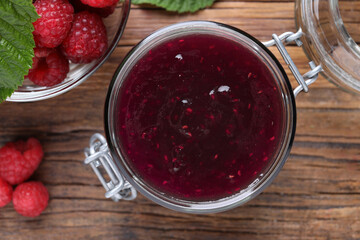 Jar of delicious raspberry jam and fresh berries on wooden table, flat lay