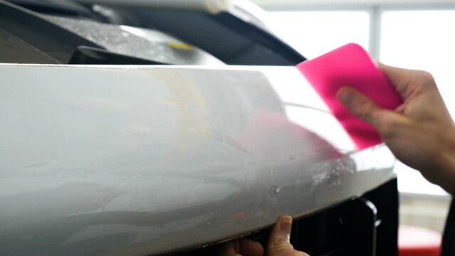 Close up of paint protection film installation on front bumper of modern luxury car. PPF is polyurethane film applied to car surface to protect the paint from stone chips, bug splatter, and abrasion.	