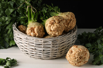 Fresh raw celery roots in wicker basket on white wooden table