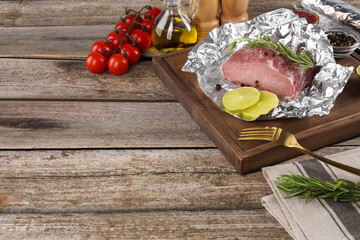 Aluminum foil with raw meat, rosemary, lime and spices on wooden table, space for text