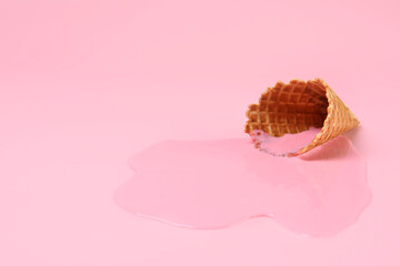 Melted ice cream and wafer cone on pink background, closeup. Space for text