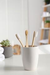 Holder with bamboo toothbrushes on white countertop in bathroom