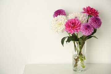 Bouquet of beautiful Dahlia flowers in vase on table near white wall, space for text - obrazy, fototapety, plakaty