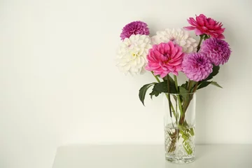 Poster Bouquet of beautiful Dahlia flowers in vase on table near white wall, space for text © New Africa