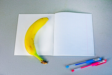 banana on the table next to a school notebook with pens. school snack
