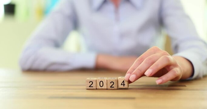 Numbers 2024 are made up of wooden cubes in row. Woman hand turned number 202 into number 2024 with finger