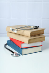 Stack of books and stethoscope on light background