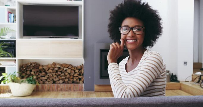 Happy, face and black woman relax on a sofa with good mood, confidence and positivity at home. Smile, portrait and African female person in a living room with me time on day off or weekend freedom