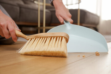 Close up image of woman's hands cleaning apartment with small broom and dustpan