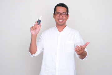 Adult Asian man smiling happy with one hand holding a car key - obrazy, fototapety, plakaty