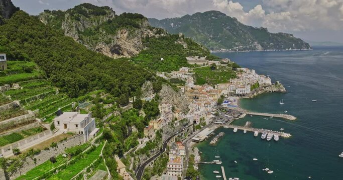 Amalfi Italy Aerial v8 cinematic fly along rocky cliff towards Mediterranean coastal town capturing terraced hillsides, waterfront harbor and pristine sea views - Shot with Mavic 3 Cine - May 2023