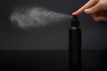 Close-up view of human hand and black spray bottle isolated on black - obrazy, fototapety, plakaty