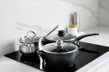The saucepans stand on an electric induction stove. Modern modernized kitchen in the style of minimalism. Kitchen interior - obrazy, fototapety, plakaty