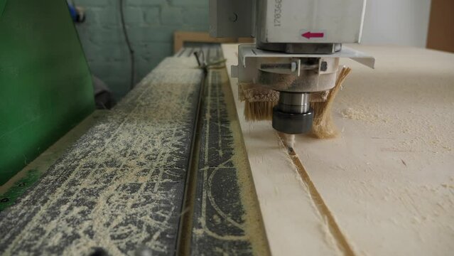 An automatic wood lathe with a drill and a connected brush cuts out parts from a sheet of plywood, industrial work in a carpentry workshop close-up. Stabilized image.