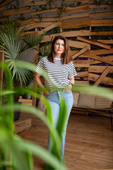 Attractive woman in casual clothes posing in room with tropical plants.