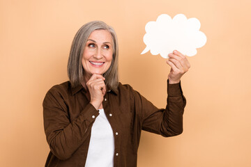Photo of minded wise woman with gray hair dressed brown shirt look at mind cloud in arm finger on chin isolated on pastel color background