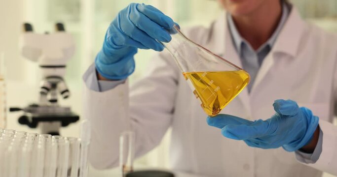 Chemist scientist pours water from transparent bottle into flask in laboratory. Scientist chemist looking at flask with yellow liquid or oil for transparency in chemical laboratory closeup