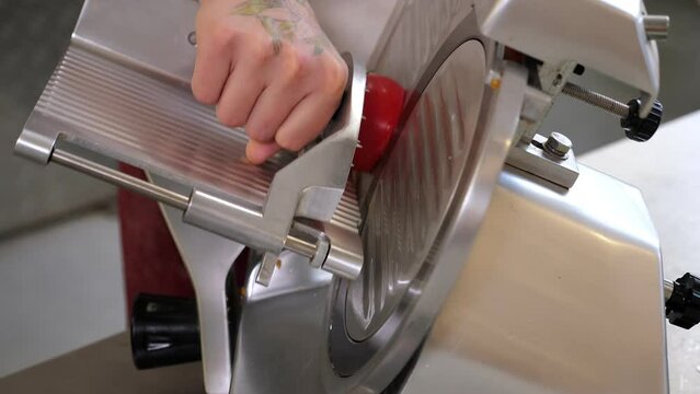 Close-up of a chef slicing sausage with an industrial meat grinder in the kitchen of a pizzeria. The production process in the restaurant kitchen. 